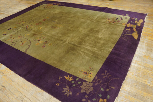 High-pile rug in olive green with a wide plum border patterned with branches and birds on a wood floor.