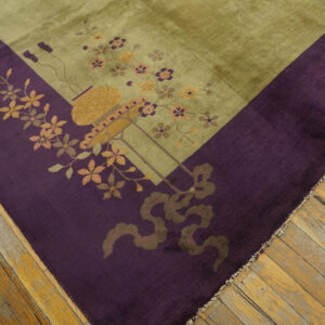 Close-up of an olive green rug with a deep purple floral border on distressed wood flooring.