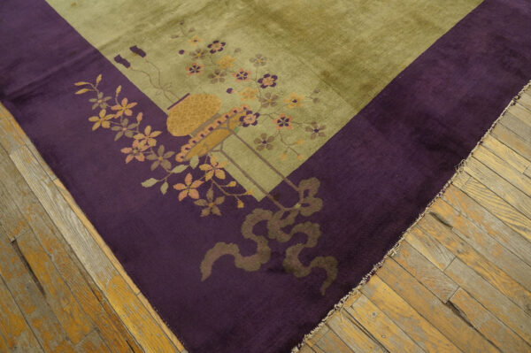 Close-up of an olive green rug with a deep purple floral border on distressed wood flooring.