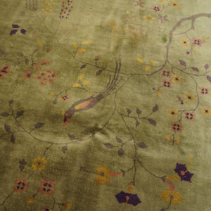 Plush olive green rug with yellow and purple floral patterns and a bird motif next to solid purple flooring.