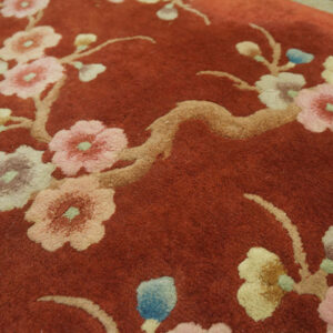 Close-up of a rust-colored high-pile rug with large floral branches; light wood floor visible behind.