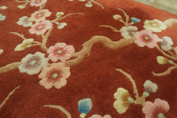Close-up of a rust-colored high-pile rug with large floral branches; light wood floor visible behind.