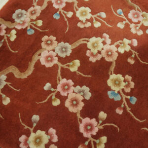 Plush, rust-colored rug with delicate pink and cream floral branches on a light wood floor.