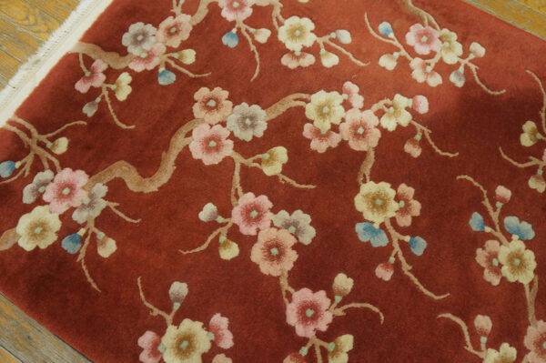 Plush, rust-colored rug with delicate pink and cream floral branches on a light wood floor.