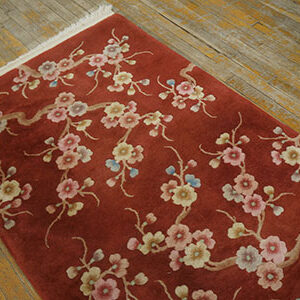 Close-up of a deep red pile rug with delicate pink and cream cherry blossom branches on distressed wood flooring.