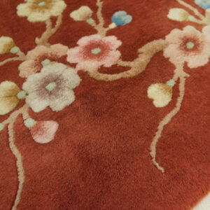 High-pile, terracotta rug detailed with sprawling branches and pastel flowers including pink, cream, and blue.