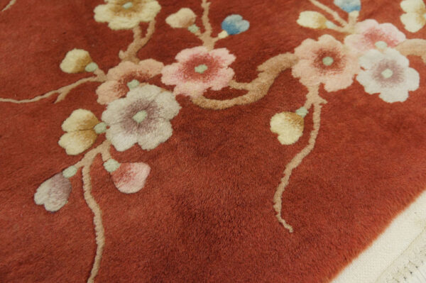 High-pile, terracotta rug detailed with sprawling branches and pastel flowers including pink, cream, and blue.
