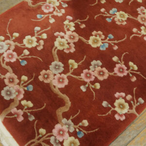 A reddish-brown rug featuring pink and yellow blossoms on tan branches on a distressed wood floor.
