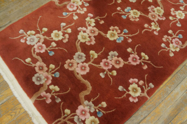 A reddish-brown rug featuring pink and yellow blossoms on tan branches on a distressed wood floor.