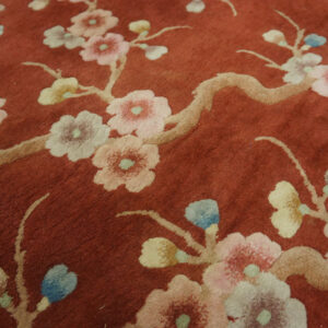 Reddish-brown rug surface featuring a raised floral branch pattern in cream, light blue, and pink pastels.