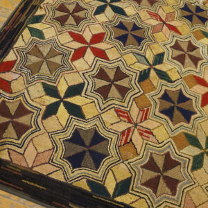 Highly textured rug with repeating multicolored star patterns surrounded by a dark brown border on wood floors.