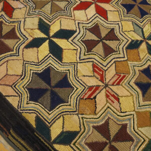 Rustic hooked rug with repeating colorful geometric stars and a dark border rests on wood flooring.