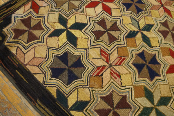 Rustic hooked rug with repeating colorful geometric stars and a dark border rests on wood flooring.