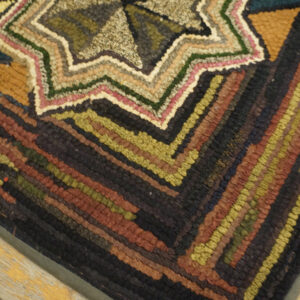 Earth-toned hooked rug with a central starburst and thick, multicolored striped borders on wood flooring.