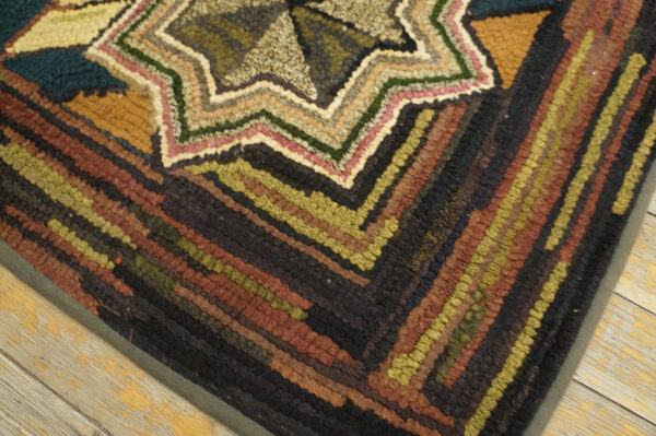 Earth-toned hooked rug with a central starburst and thick, multicolored striped borders on wood flooring.