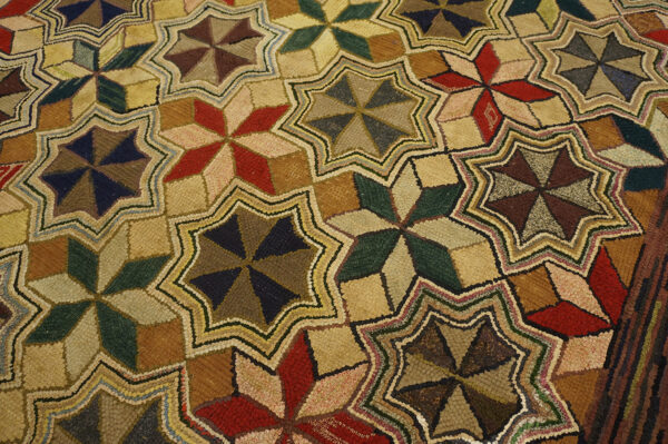 Textured rug featuring geometric, multi-colored pinwheel stars arranged in an interlocking, zigzagging tan grid.