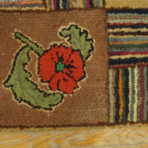 Hooked patchwork rug with a red and green flower centered on brown, bordered by multicolor stripes.