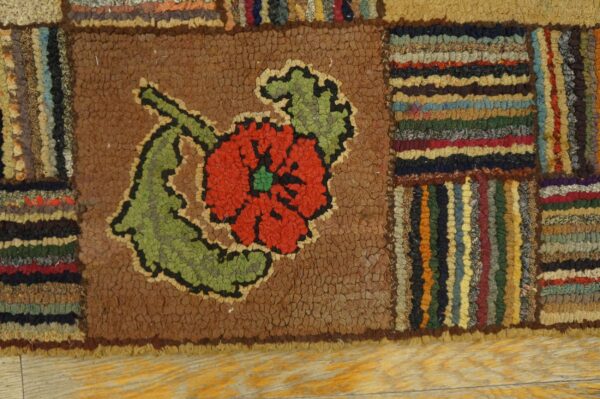 Hooked patchwork rug with a red and green flower centered on brown, bordered by multicolor stripes.
