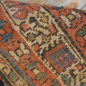 Close-up shows a folded geometric rug with red, tan, blue, and black patterns resting on wood.