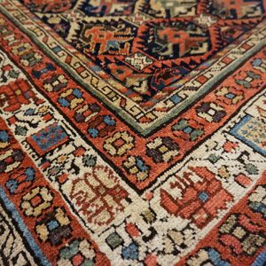 Detailed view of a low-pile rug corner with intricate geometric borders in rust, navy, cream, and green.