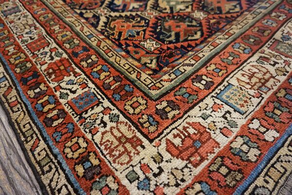 Detailed view of a low-pile rug corner with intricate geometric borders in rust, navy, cream, and green.