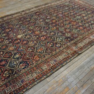 Multicolored rug with a dense geometric pattern and complex borders rests on distressed, gray wooden planks.