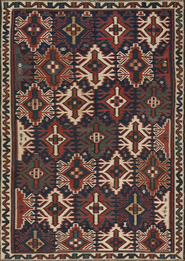 Geometric flat woven rug displaying repeating patterns in navy blue, rusty red, cream, and teal accents.