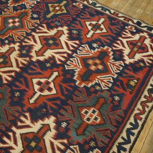 Geometric flatweave rug featuring navy, terracotta, cream, and green patterns, resting on wood flooring.