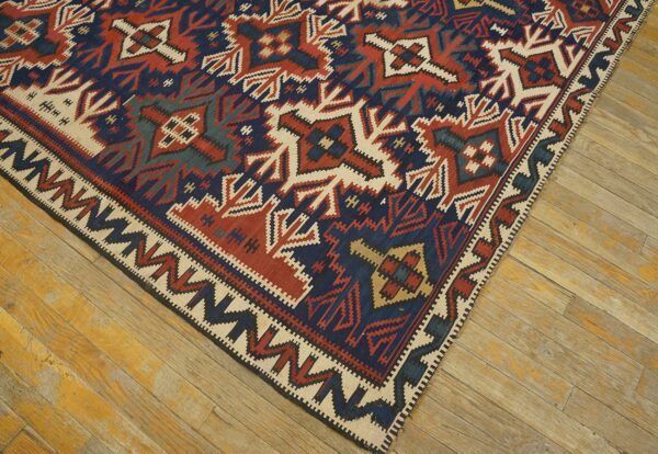 Red, navy, and cream geometric flatweave rug lying diagonally on worn, light-toned wood flooring.