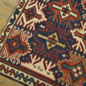 Geometric flat-weave rug in navy, brick red, and ivory colors resting on rustic wood planks.