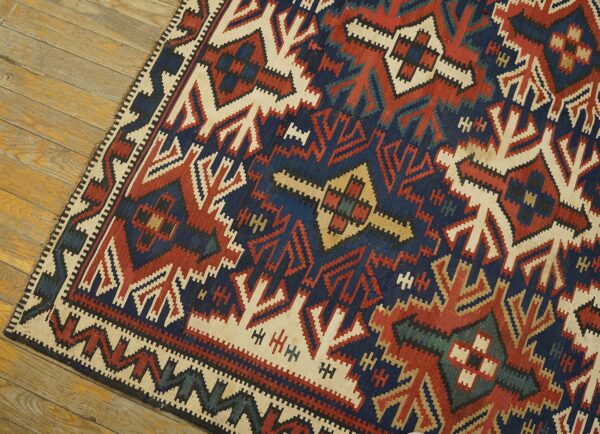 Geometric flat-weave rug in navy, brick red, and ivory colors resting on rustic wood planks.