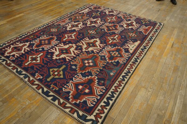 Flatweave rug with large geometric motifs in navy, rust red, and cream on worn wood floors.