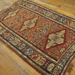 Red-orange and navy tribal rug with geometric patterns and fringe lies on light brown hardwood flooring.