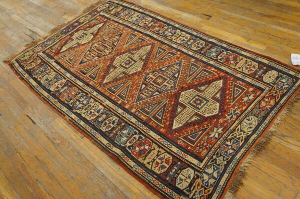 Red-orange and navy tribal rug with geometric patterns and fringe lies on light brown hardwood flooring.