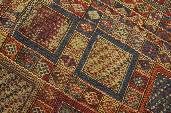 A colorful, flatweave, geometric pattern featuring complex diamonds in red, deep blue, gold, and orange threads.