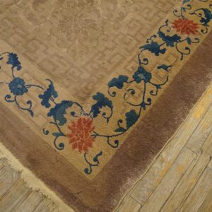 The corner of a beige rug displays a dark blue and coral floral border over weathered wood flooring.