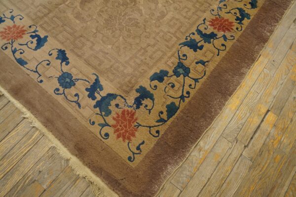 The corner of a beige rug displays a dark blue and coral floral border over weathered wood flooring.