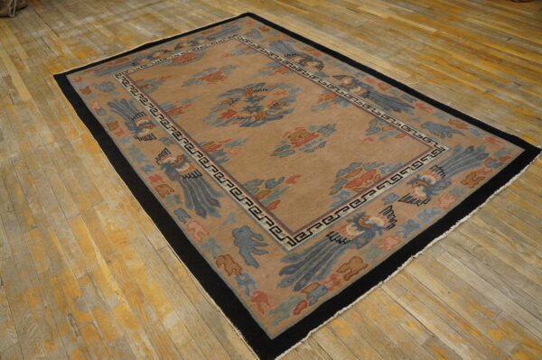 Low pile tan rug with stylized blue and coral bird patterns and thick black borders on wide wood planks.
