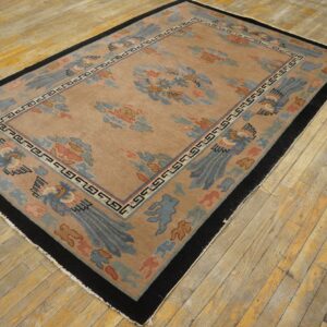 Tan rug with light blue and coral stylized bird and cloud patterns, bordered in black, laid on worn hardwood flooring.