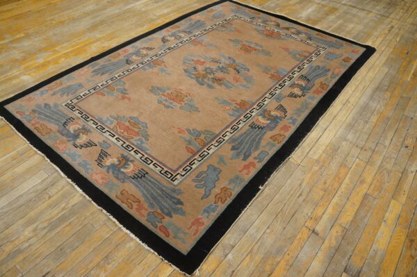 Tan rug with light blue and coral stylized bird and cloud patterns, bordered in black, laid on worn hardwood flooring.