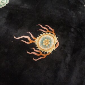 Plush black rug with a stylized yellow and blue medallion surrounded by pink and orange tendrils.