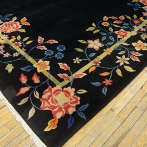 Low-pile black rug featuring colorful floral vines and yellow stems, with white fringe on worn wood flooring.