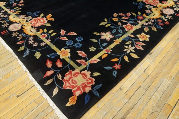 Low-pile black rug featuring colorful floral vines and yellow stems, with white fringe on worn wood flooring.