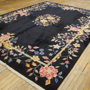 Black rug with a pale yellow-framed border filled with pink and blue floral elements on wood floor.