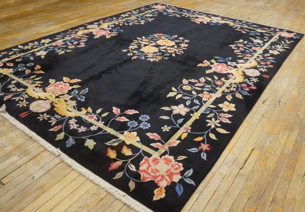 Black rug with a pale yellow-framed border filled with pink and blue floral elements on wood floor.