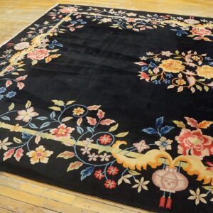 Ornate black rug with vibrant pink, yellow, and blue floral motifs laid out on wide plank wood flooring.