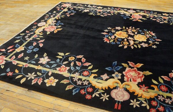 Ornate black rug with vibrant pink, yellow, and blue floral motifs laid out on wide plank wood flooring.