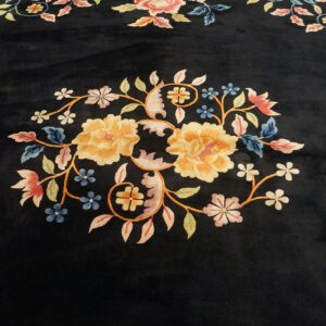 Dark, low-pile rug featuring an ornate central floral design in gold, pink, blue, and green colors.