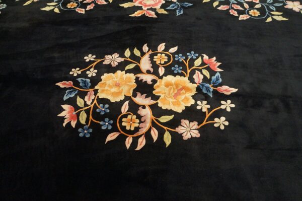 Dark, low-pile rug featuring an ornate central floral design in gold, pink, blue, and green colors.