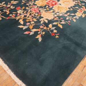 A velvety teal rug featuring large pink and yellow floral sprays is displayed on light plank wood flooring.